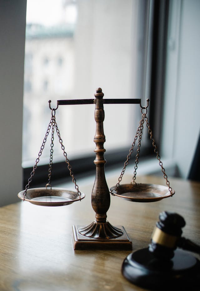 A scale and gavel sit on a judge’s wooden desk in a dark room with only sunlight coming in through a small window, highlighting the current obscurity of ethics in artificial intelligence which needs to be highlighted much more extensively.