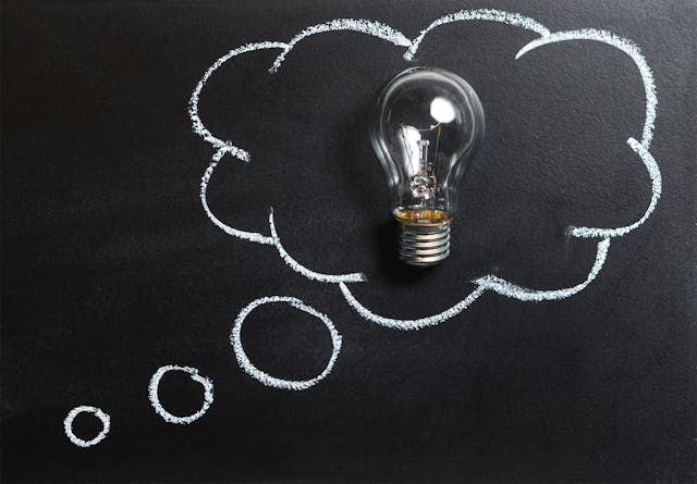 A light bulb inside a chalk-drawn thought bubble on a black background symbolizes innovative ideas and problem-solving with artificial intelligence